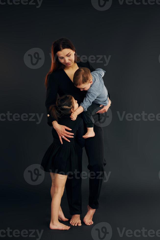 Woman in black stylish clothes is with her little son and daughter in the studio photo