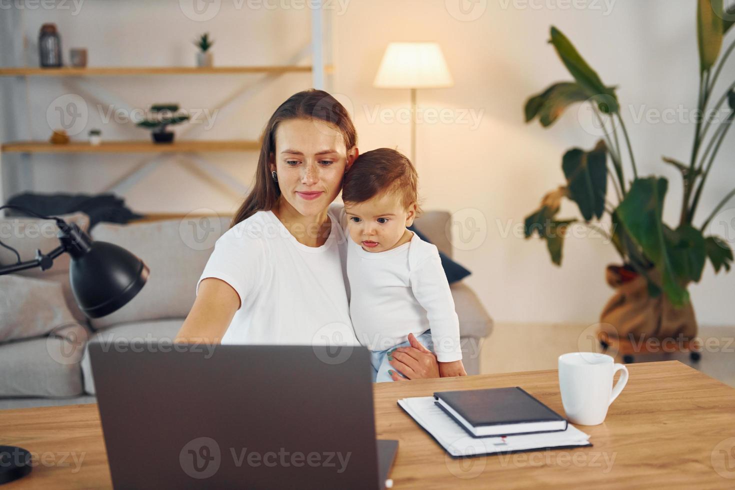 Sitting by the table with laptop. Mother with her little daughter is at home together photo