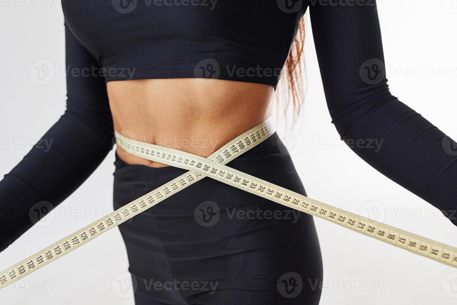 Close up view of sportive woman with measuring tape in the studio against white background photo