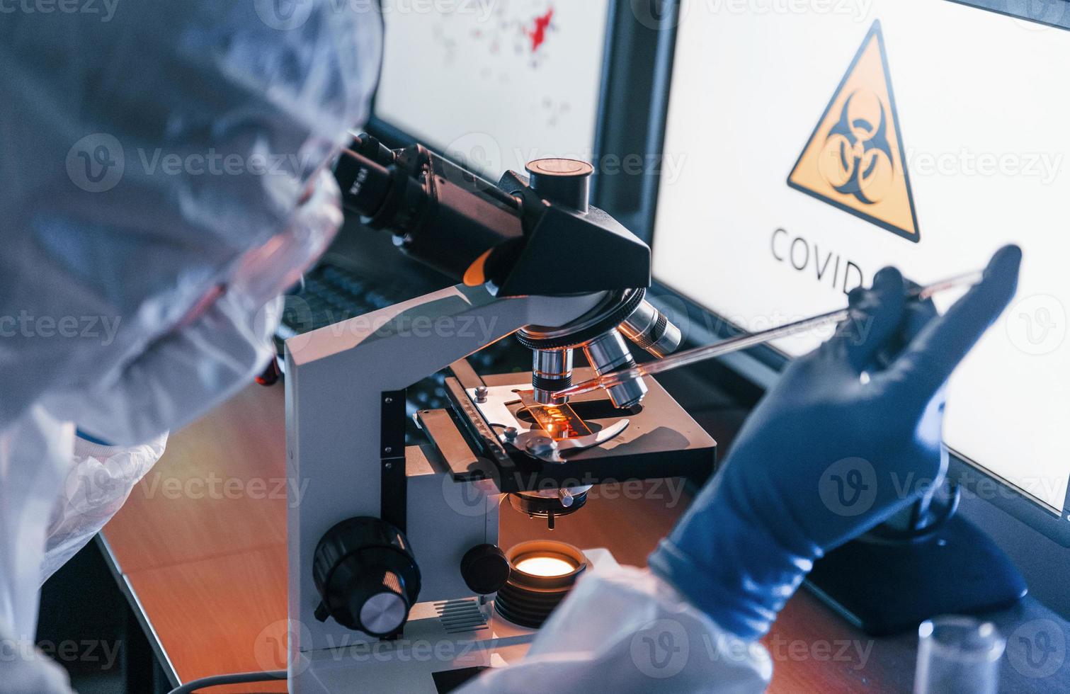 científico con uniforme protector blanco trabaja con coronavirus y tubos de sangre en laboratorio foto