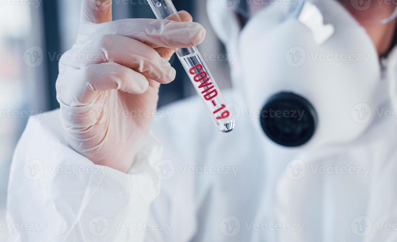 Red COVID-19 word. Nurse in protective uniform, mask and glasses standing indoors photo