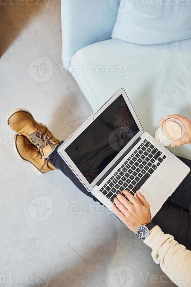 Close up view of man that works by laptop indoors by the sofa photo