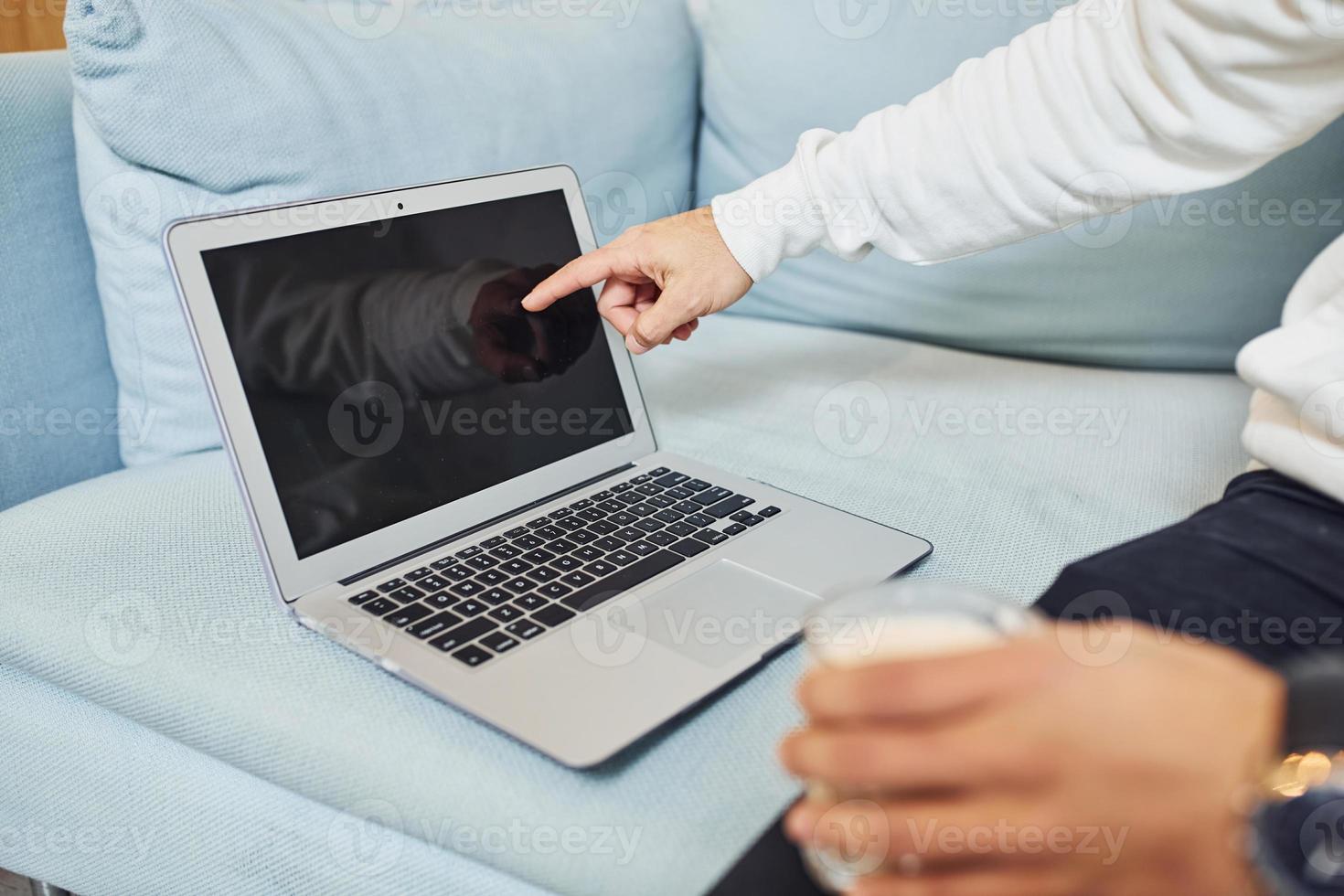 Close up view of man that works by laptop indoors by the sofa photo