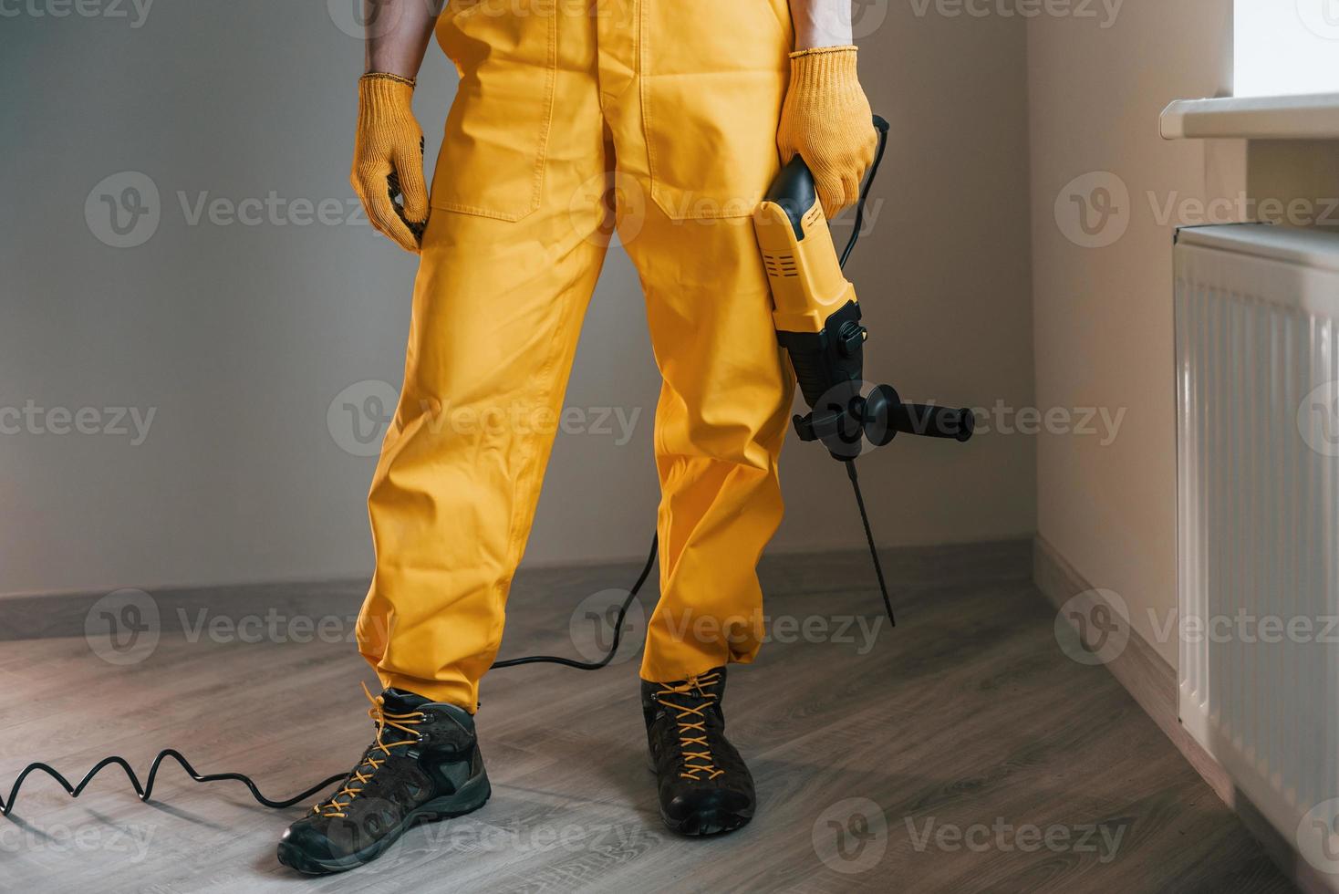 Handyman in yellow uniform with drill standing indoors. House renovation conception photo