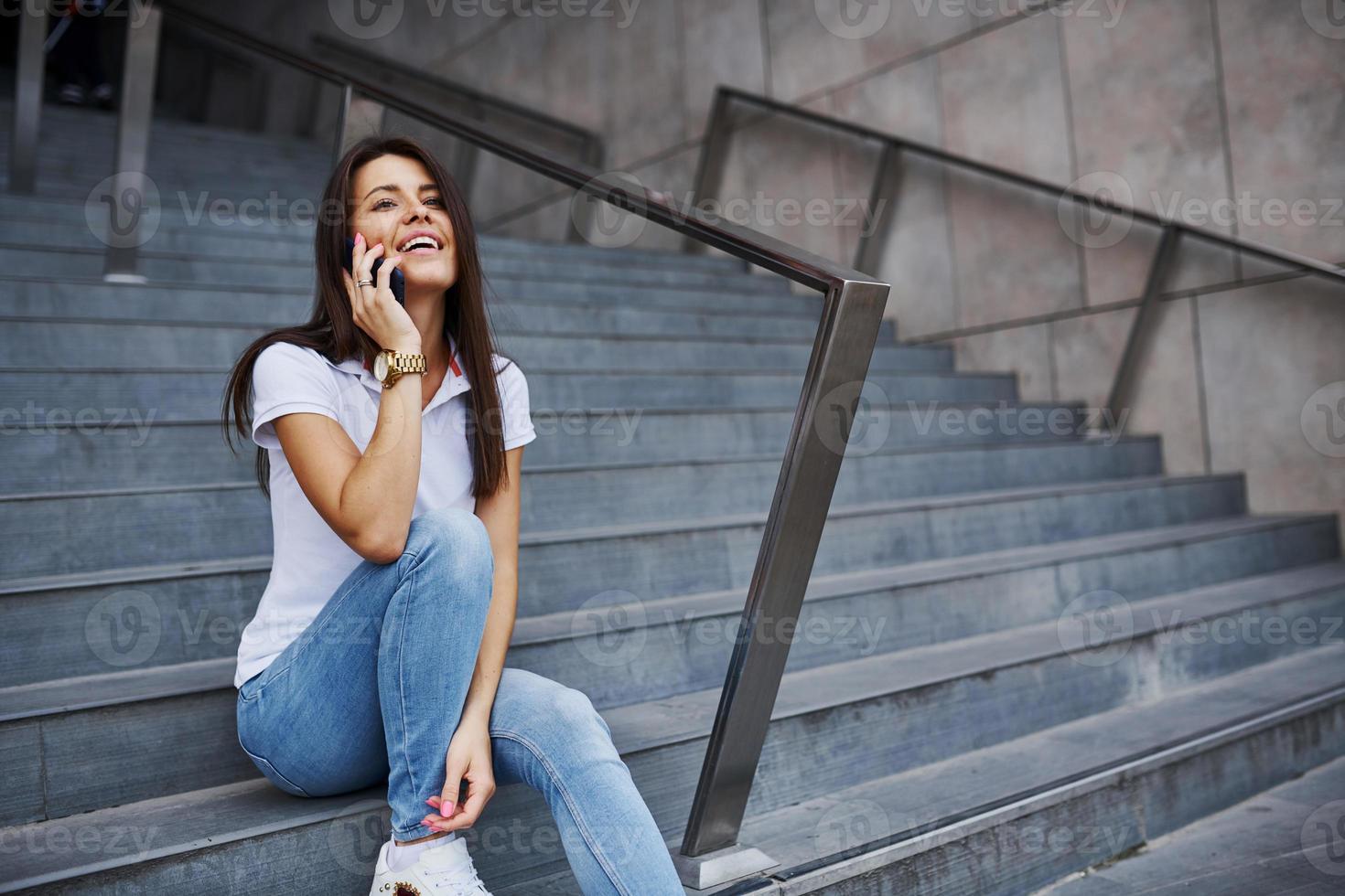 sentado en las escaleras con el teléfono inteligente en las manos. una mujer muy joven tiene un fin de semana en la ciudad durante el día foto