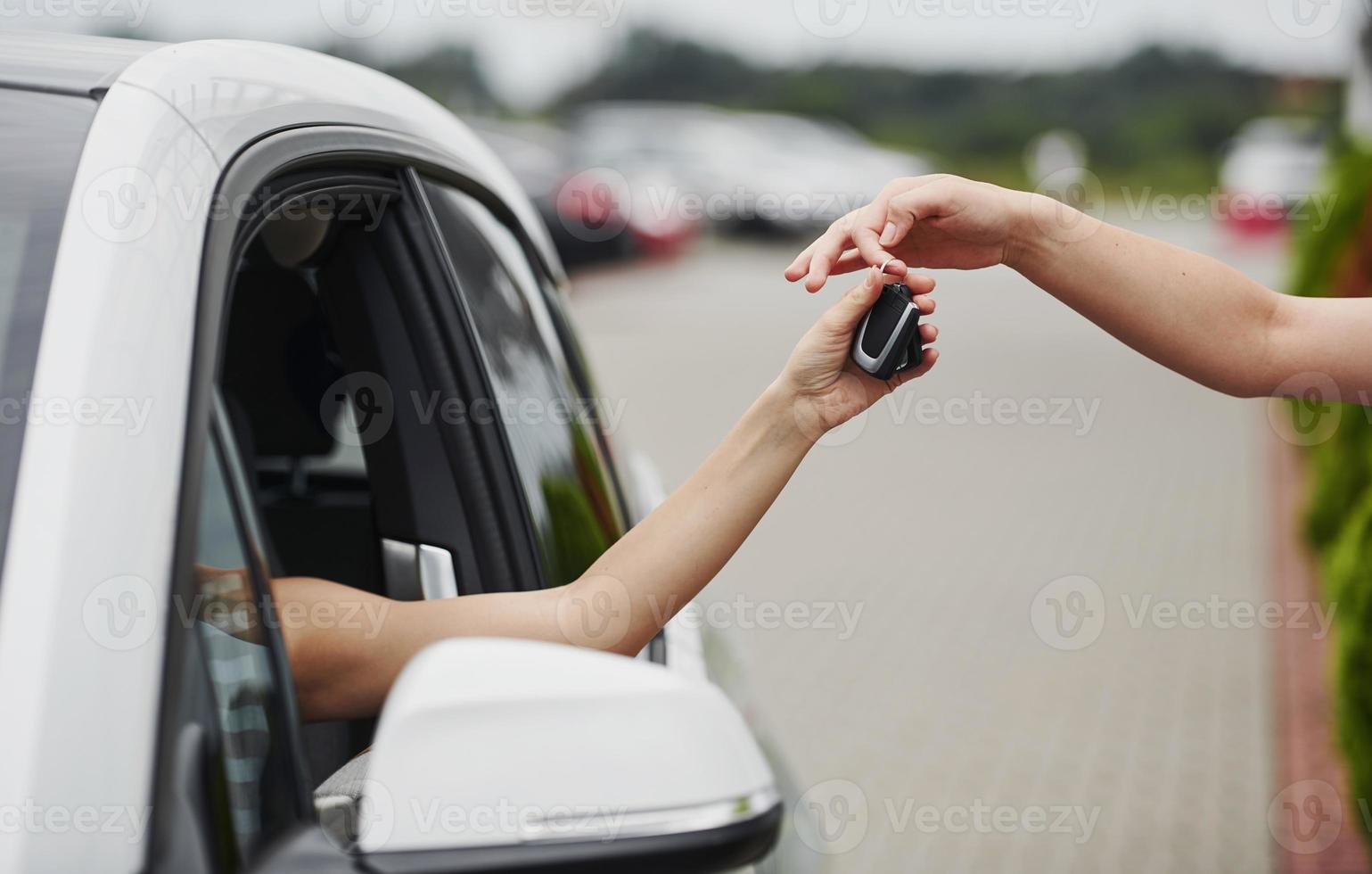 Taking keys of the car. Two people. Girl sitting in her brand new automobile photo