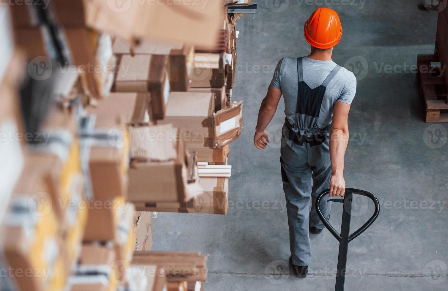 Young male worker in uniform is in the warehouse with pallet truck photo