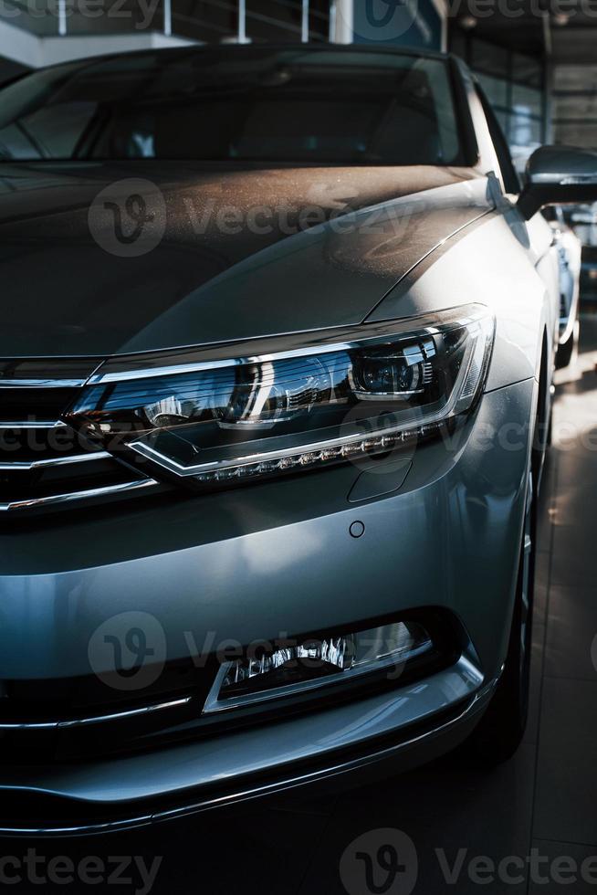 Front part of brand new modern car. Parked at showroom. Reflection in the headlights photo