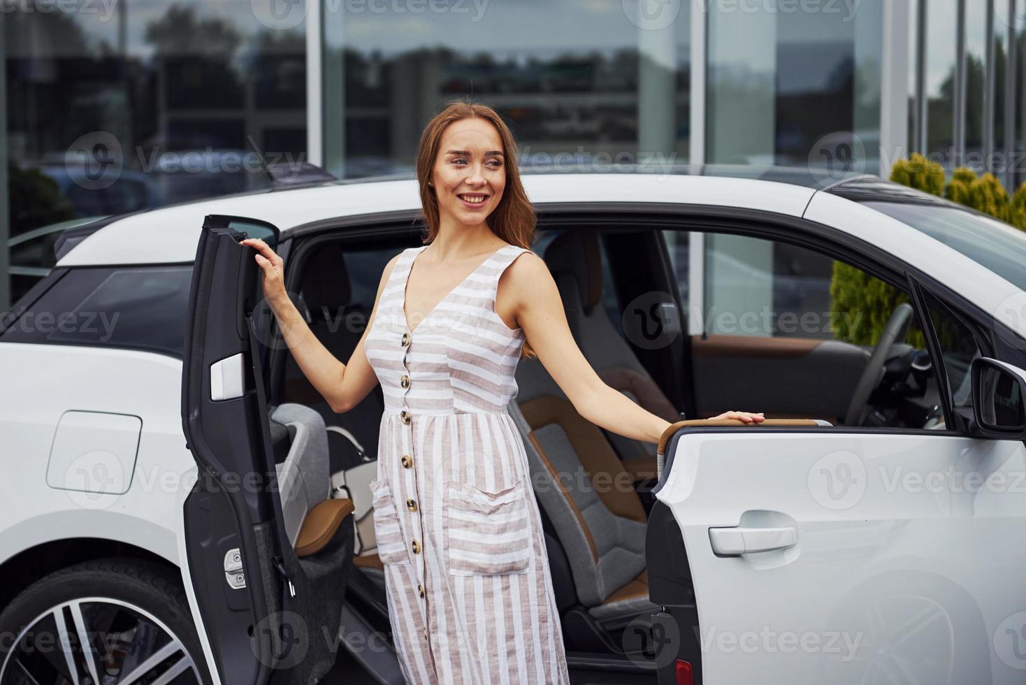 Woman with blonde hair stands near her white car on the street photo