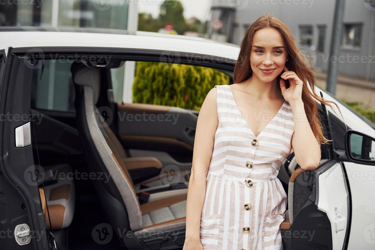 Woman with blonde hair stands near her white car on the street photo