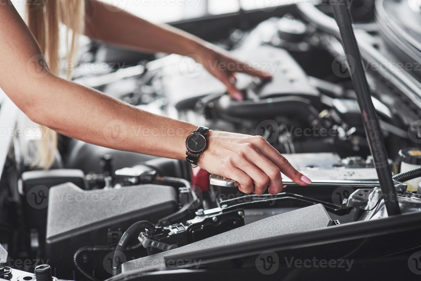 Black watch on hand. Car addicted woman repairs black car indoors in garage at daytime photo