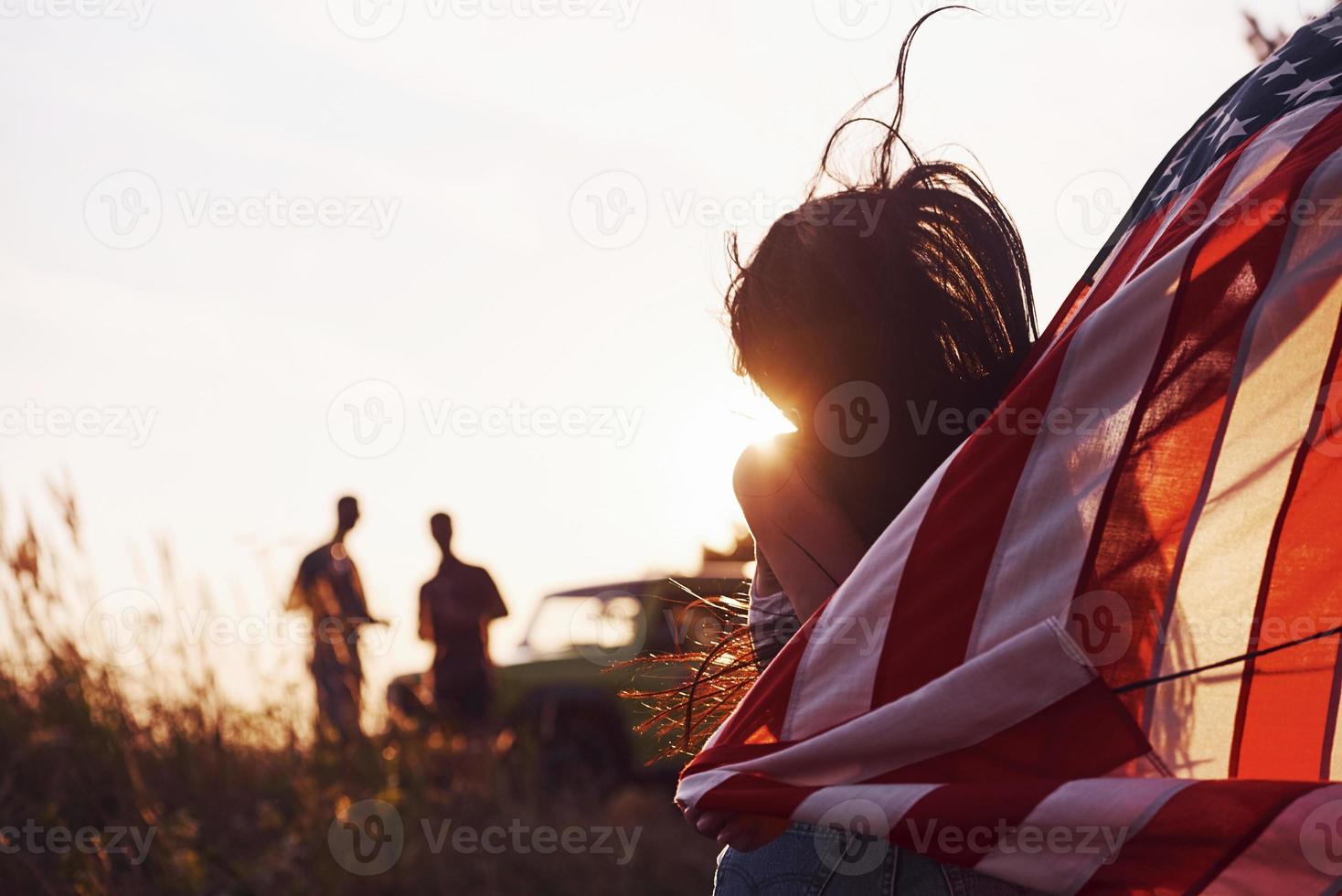 chica frente a la gente. los amigos tienen un buen fin de semana al aire libre cerca de su auto verde con bandera de estados unidos foto