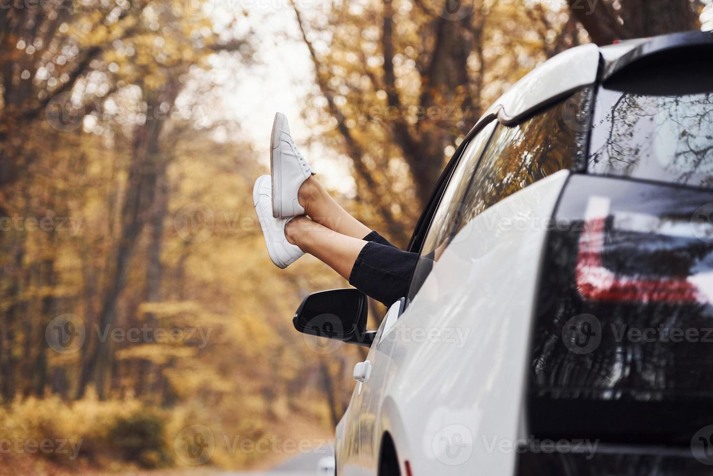 las piernas de la mujer están fuera de la ventana del auto. automóvil nuevo y moderno en el bosque foto