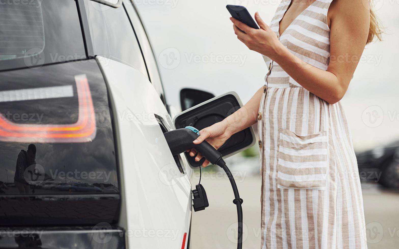 Woman on the electric cars charge station at daytime. Brand new vehicle photo