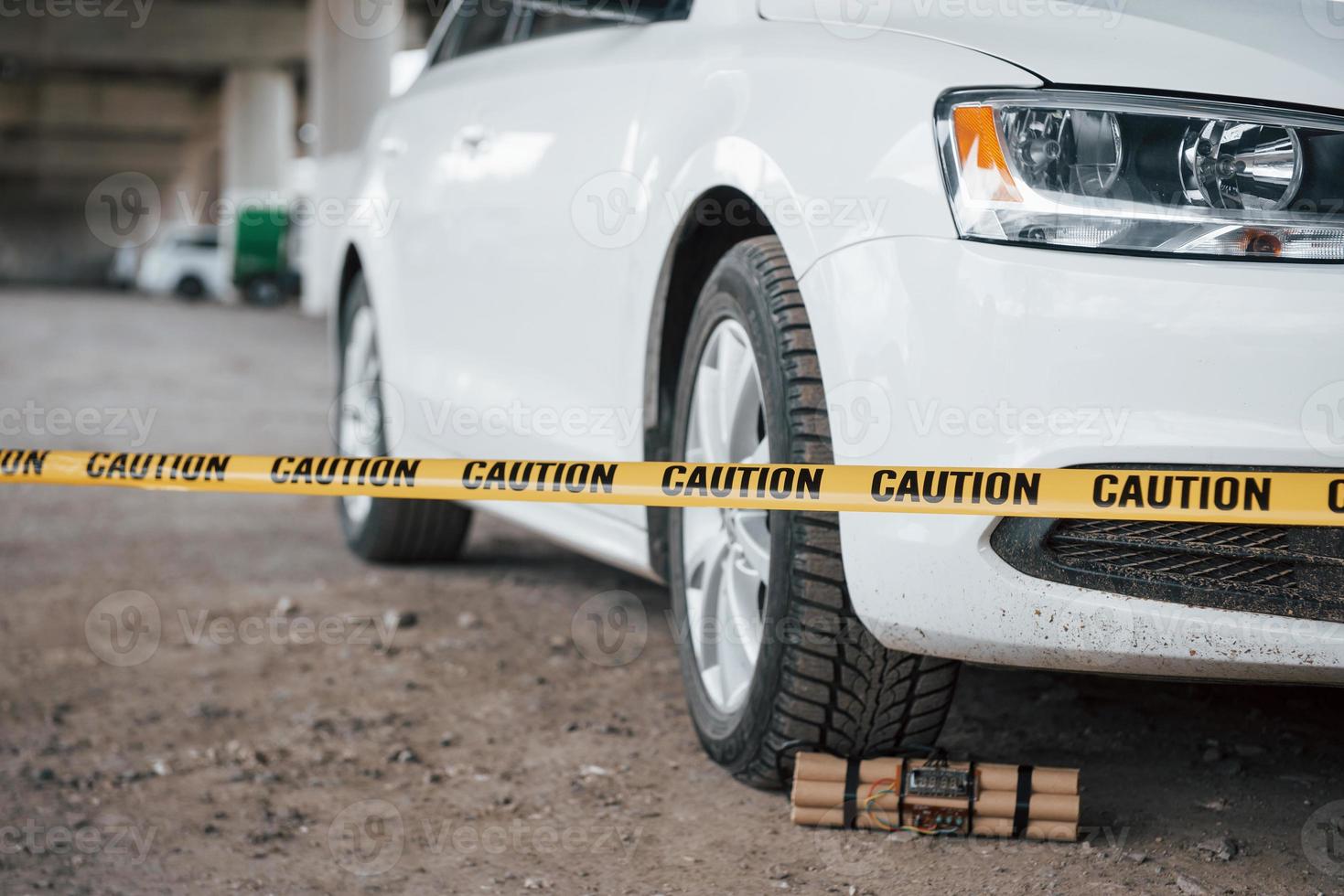 ten cuidado, es peligroso. explosivo cerca de la rueda del coche blanco moderno. cinta amarilla de precaución en el frente foto