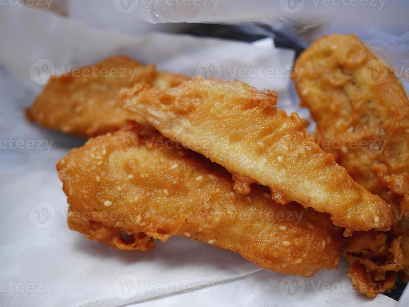 Close up Golden brown Banana fritters on the fried oil blotting paper, Thai street food, selective focus photo