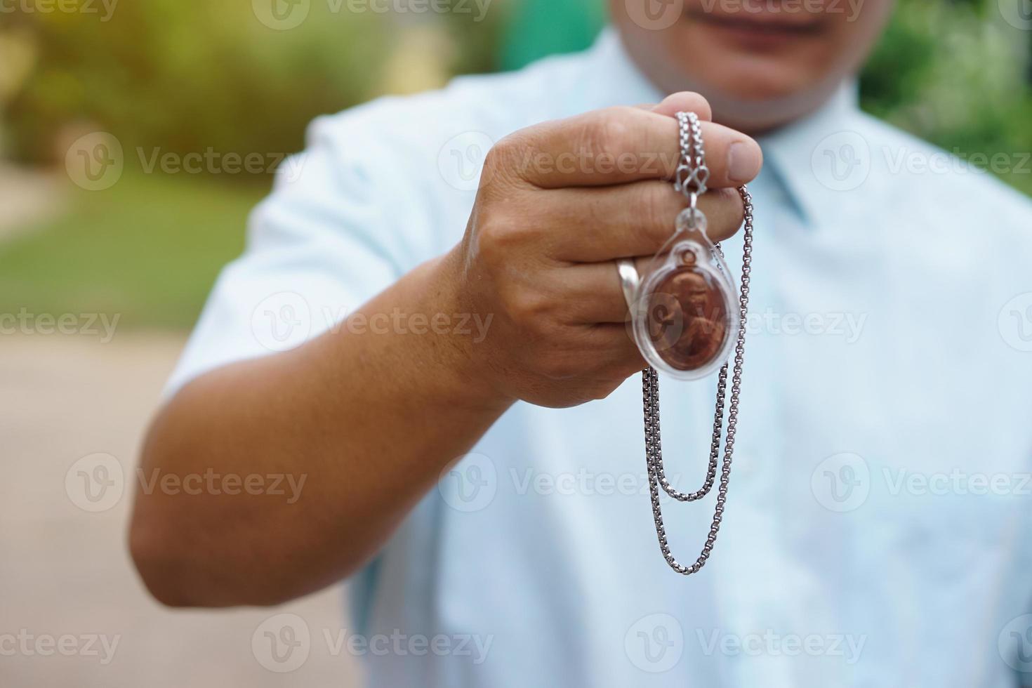 Closeup man in blue shirt holds Thai Buddha amulet necklace.  Concept, faith and belief of Buddhist for holy to protect from dangers, bring good luck, business prosperity and wealth. photo