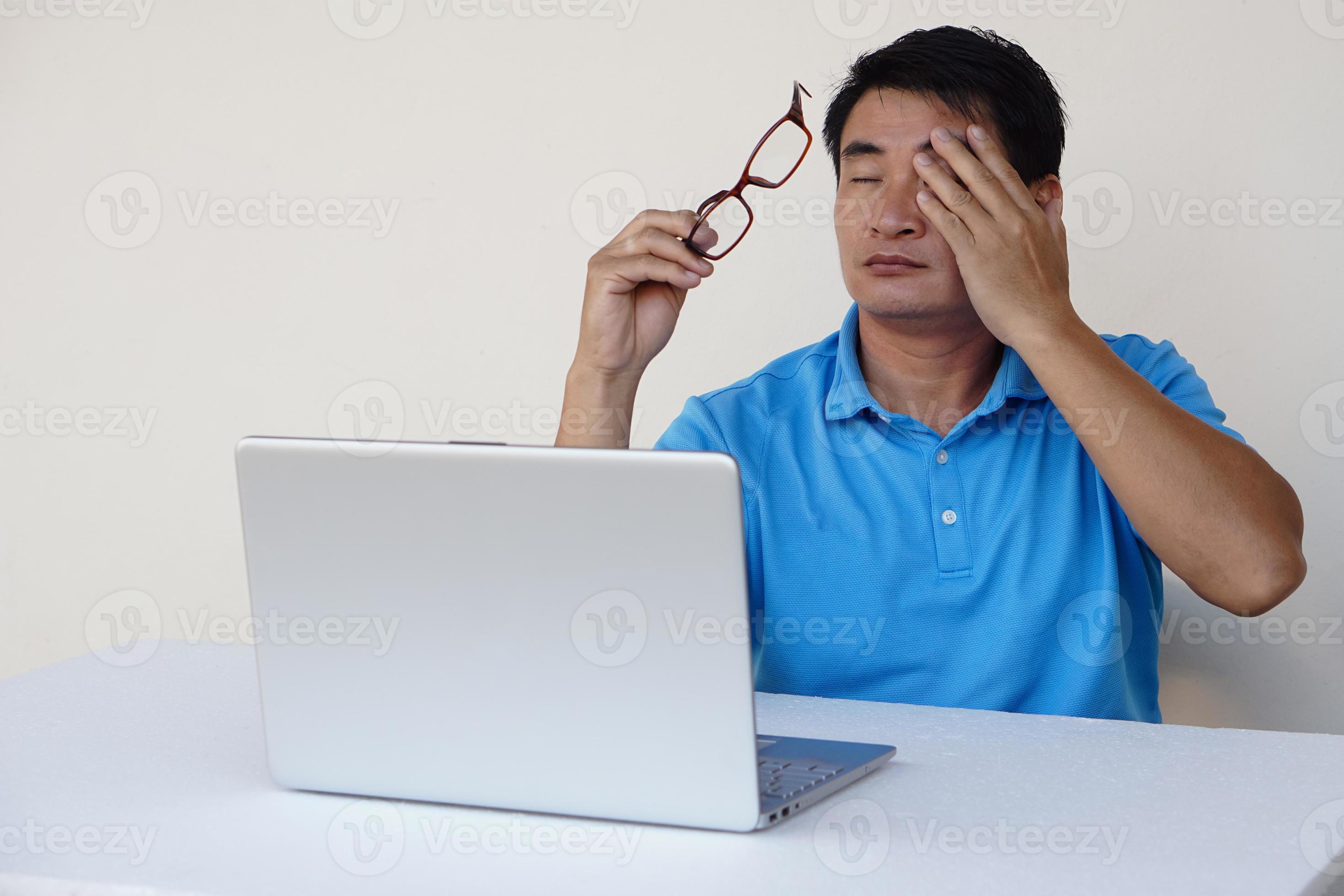 Asian man, feels hurt his eyes, holds eyeglasses during working on