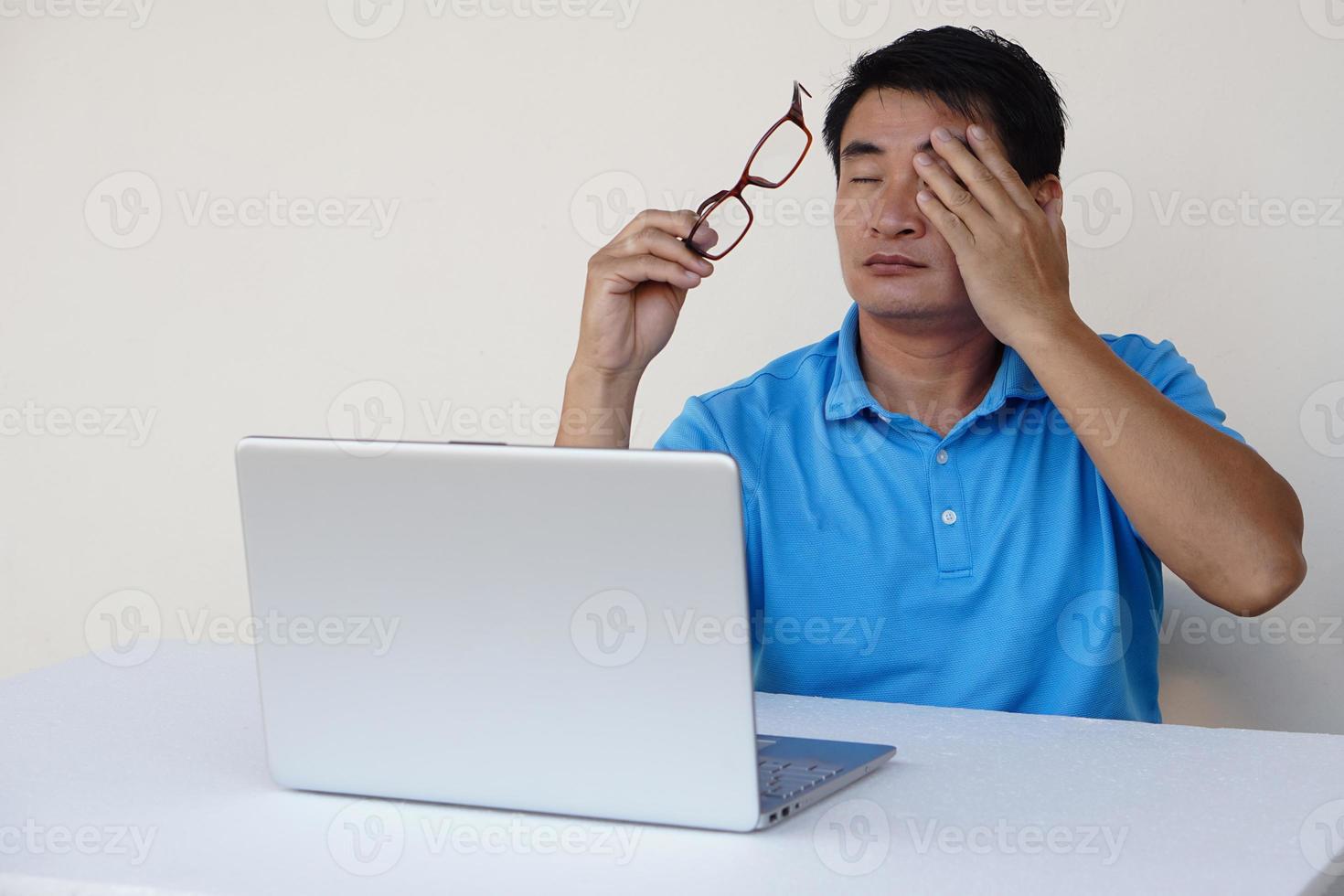 Asian man, feels hurt his eyes, holds eyeglasses during working on laptop. concept , Eyesight problem. Optometry. Glasses with convex or concave lenses. Myopia.Eye disease photo