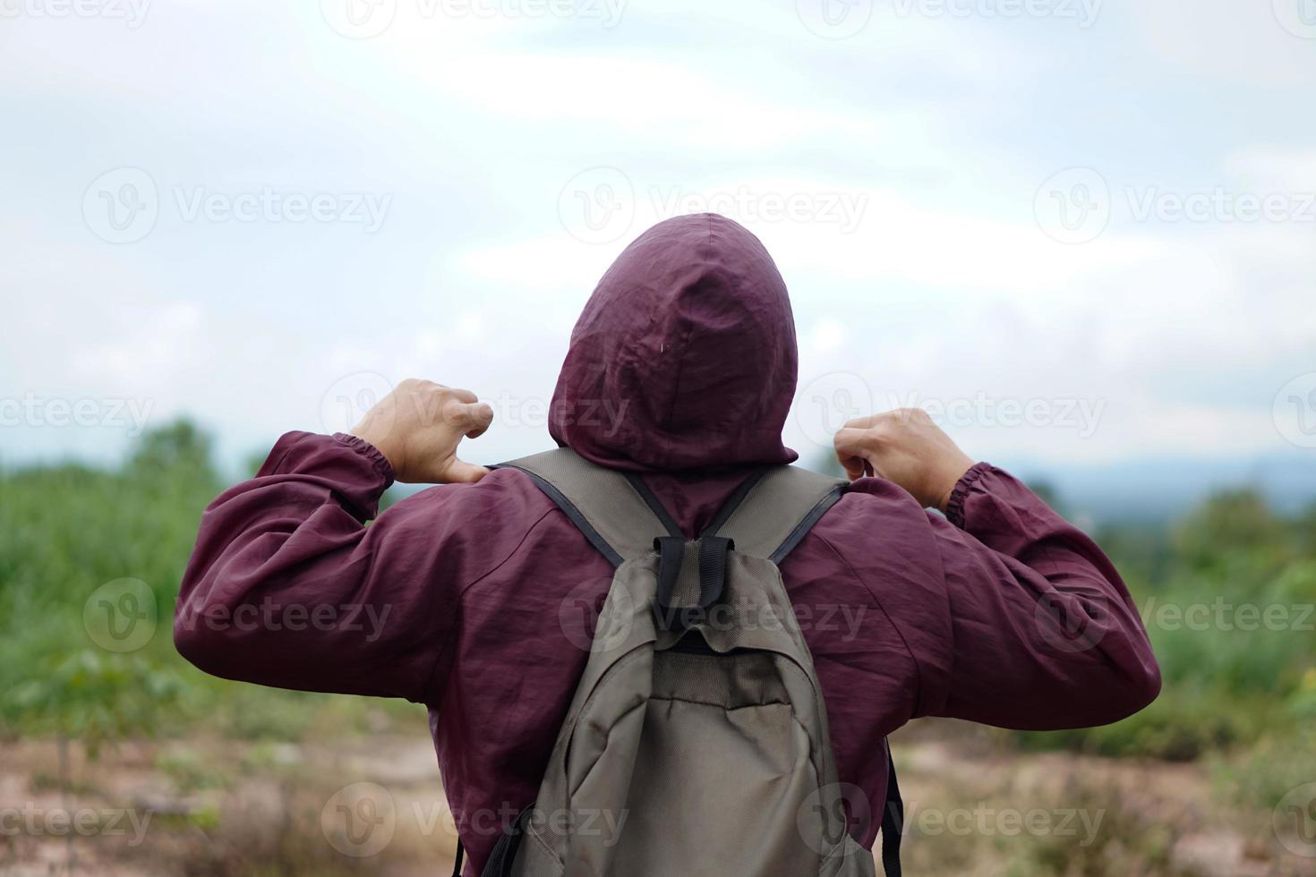 Back View of man wears brown hoodie cloth and backpack, stand outdoor, enjoy nature sightseeing. Concept, travelling alone,  happy and freedom travel on holiday vacation. photo