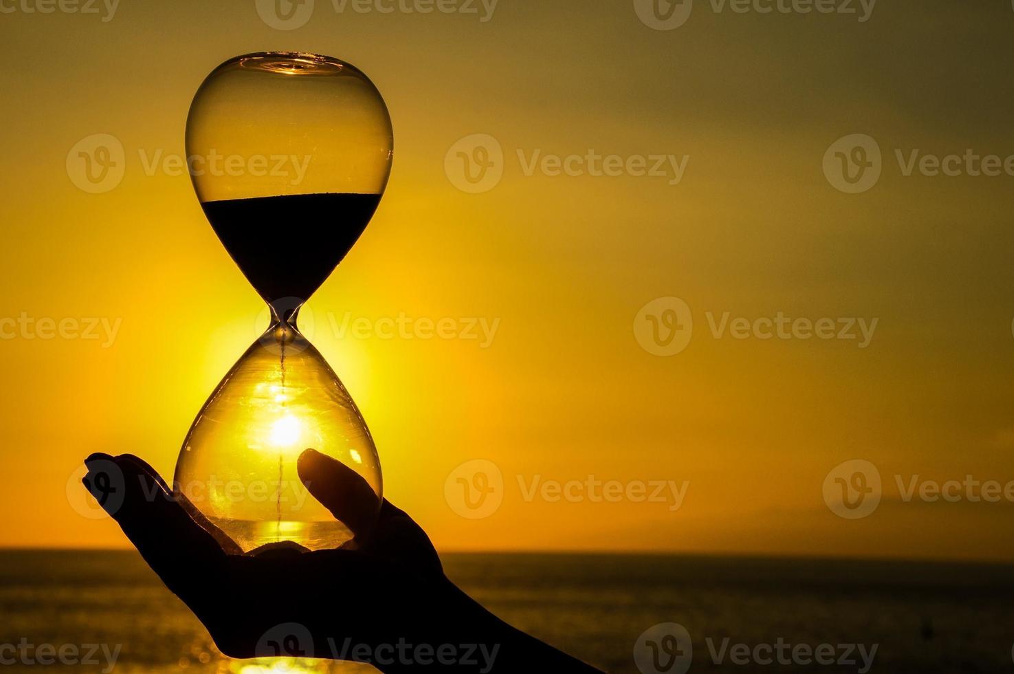 Hand holding hourglass on sunset photo