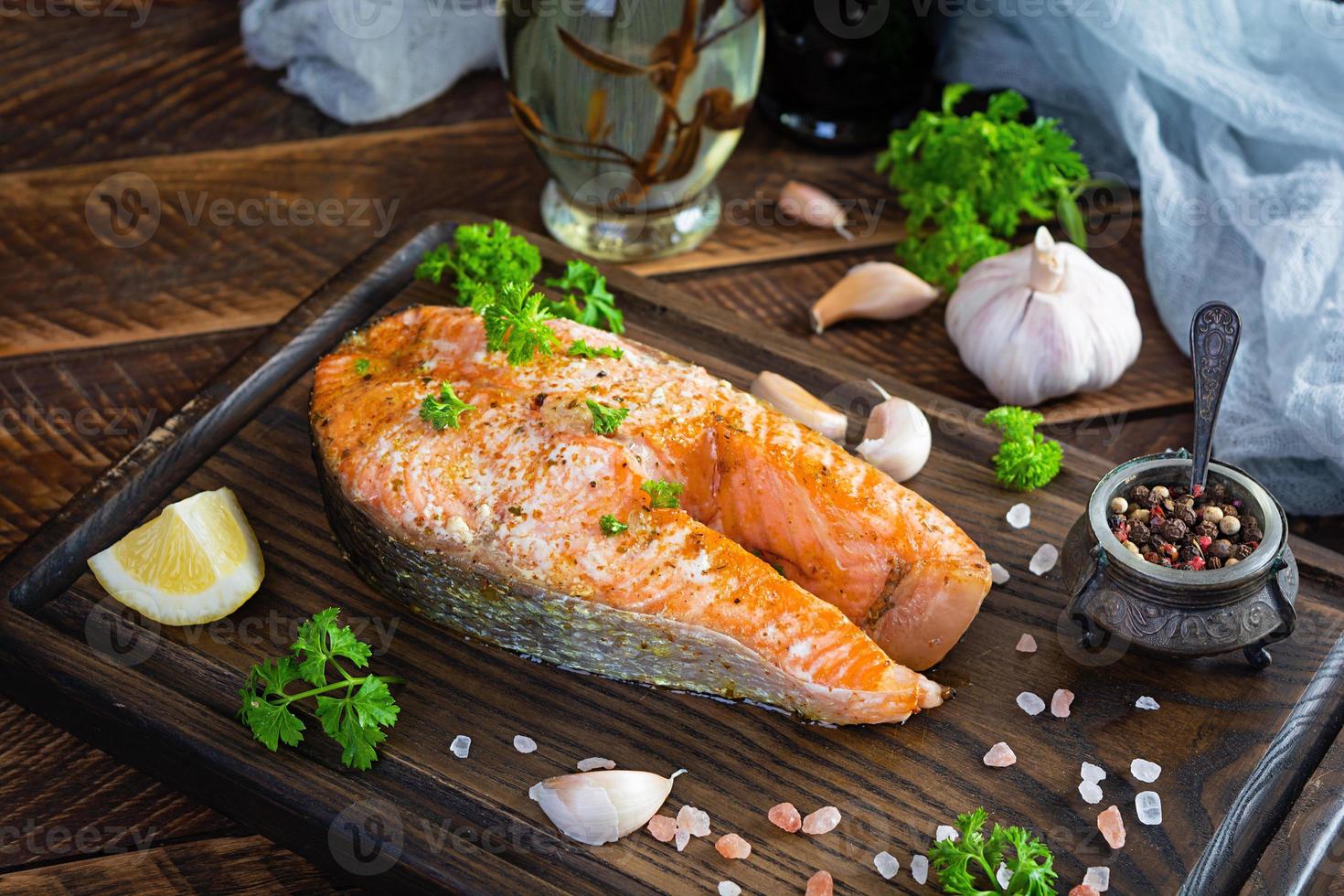 Baked salmon steak with herbs on wooden cutting board. Grilled salmon with salt and pepper photo