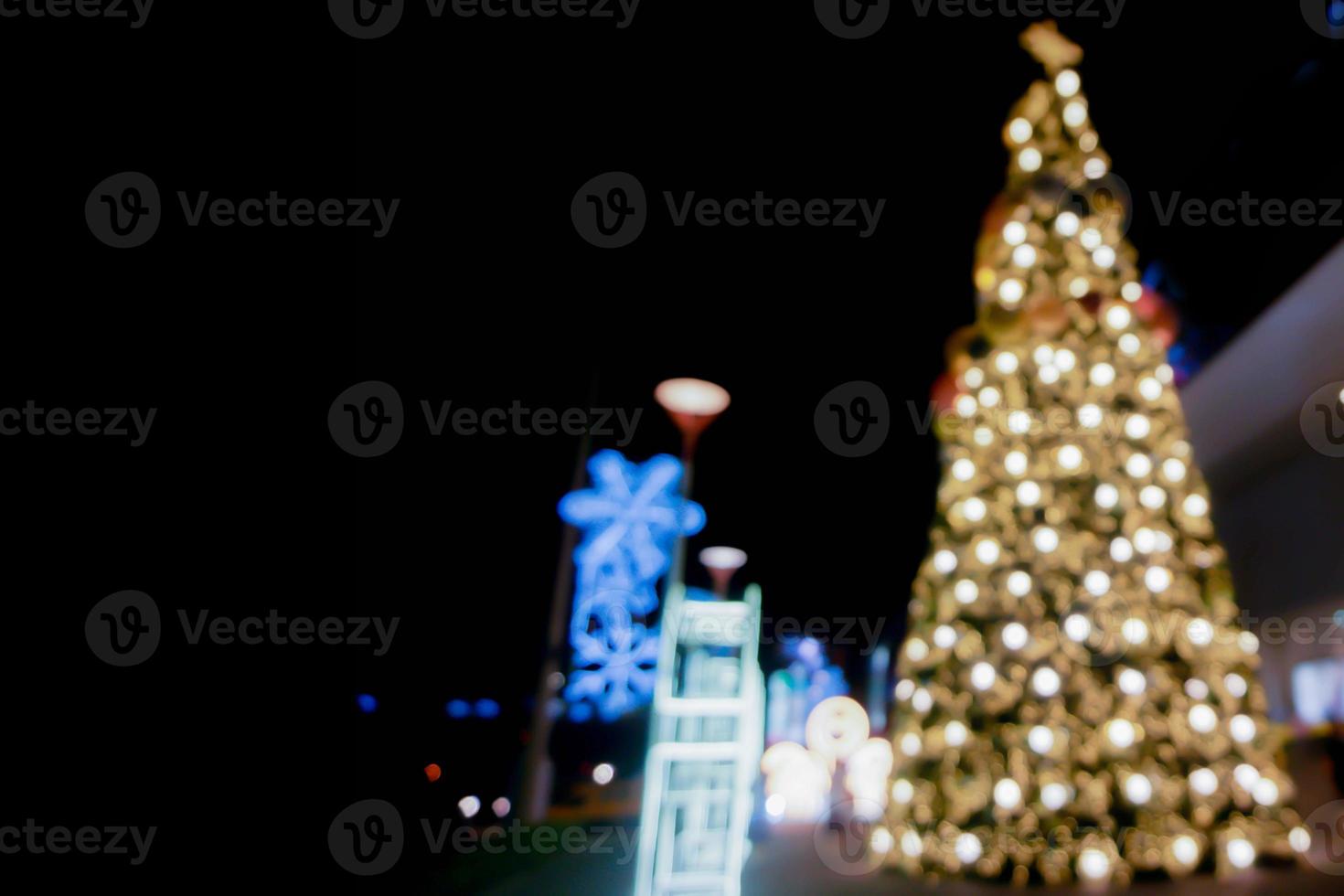 vista borrosa y bokeh del árbol de navidad y decorar la iluminación led frente al centro comercial en la noche de navidad en la ciudad urbana. foto