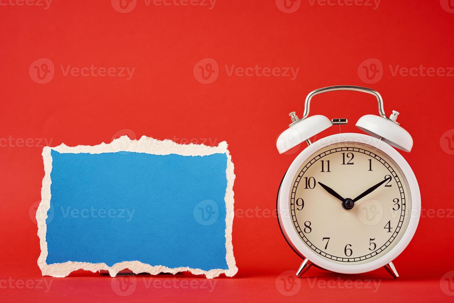 Classic alarm clock with bells and empty torn paper sheet on the red background. photo