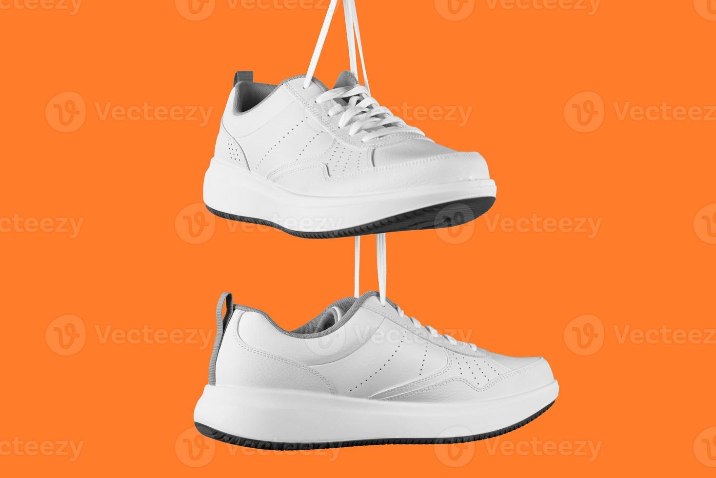 Pair of white male sneakers on orange background. photo