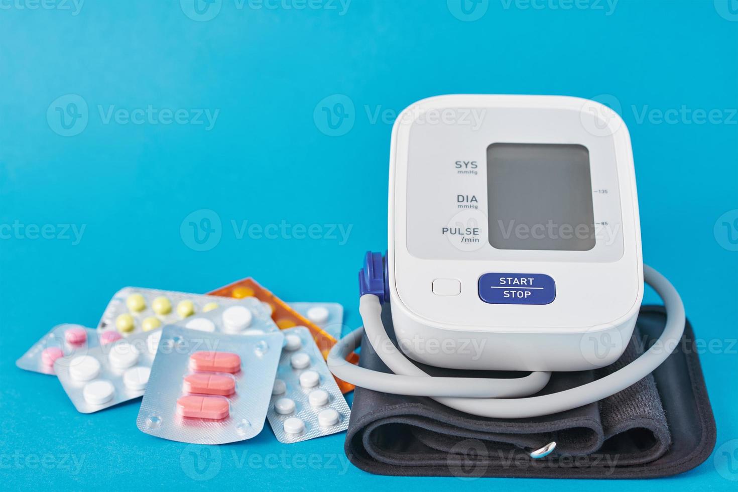 Digital blood pressure monitor and medical pills on a blue background photo