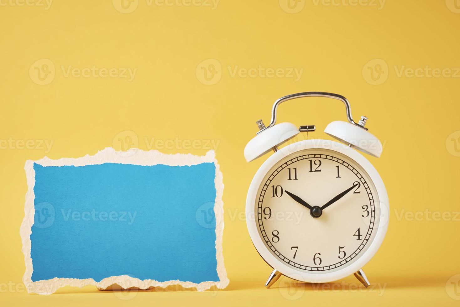 Classic alarm clock with bells and empty torn paper sheet on yellow background photo