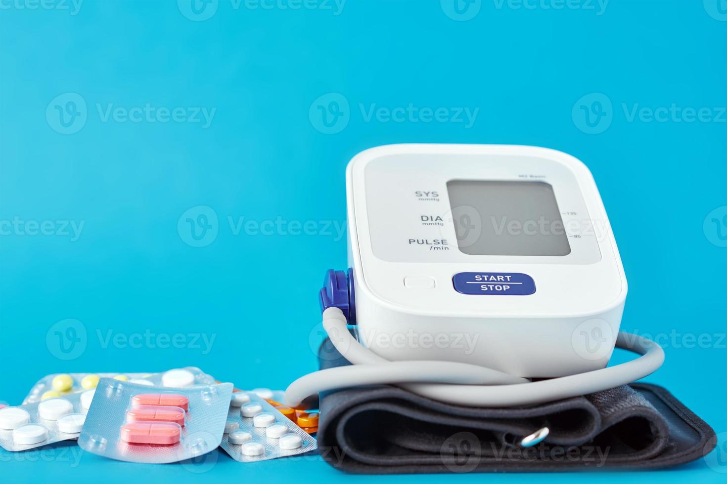 Digital blood pressure monitor and medical pills on a blue background photo