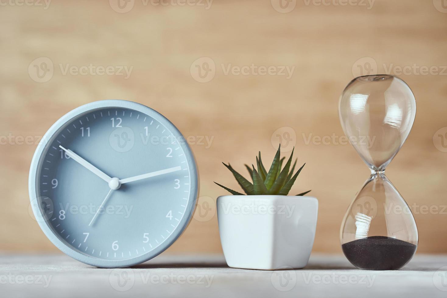 Hourglass, alarm clock and plant on the table, close up photo
