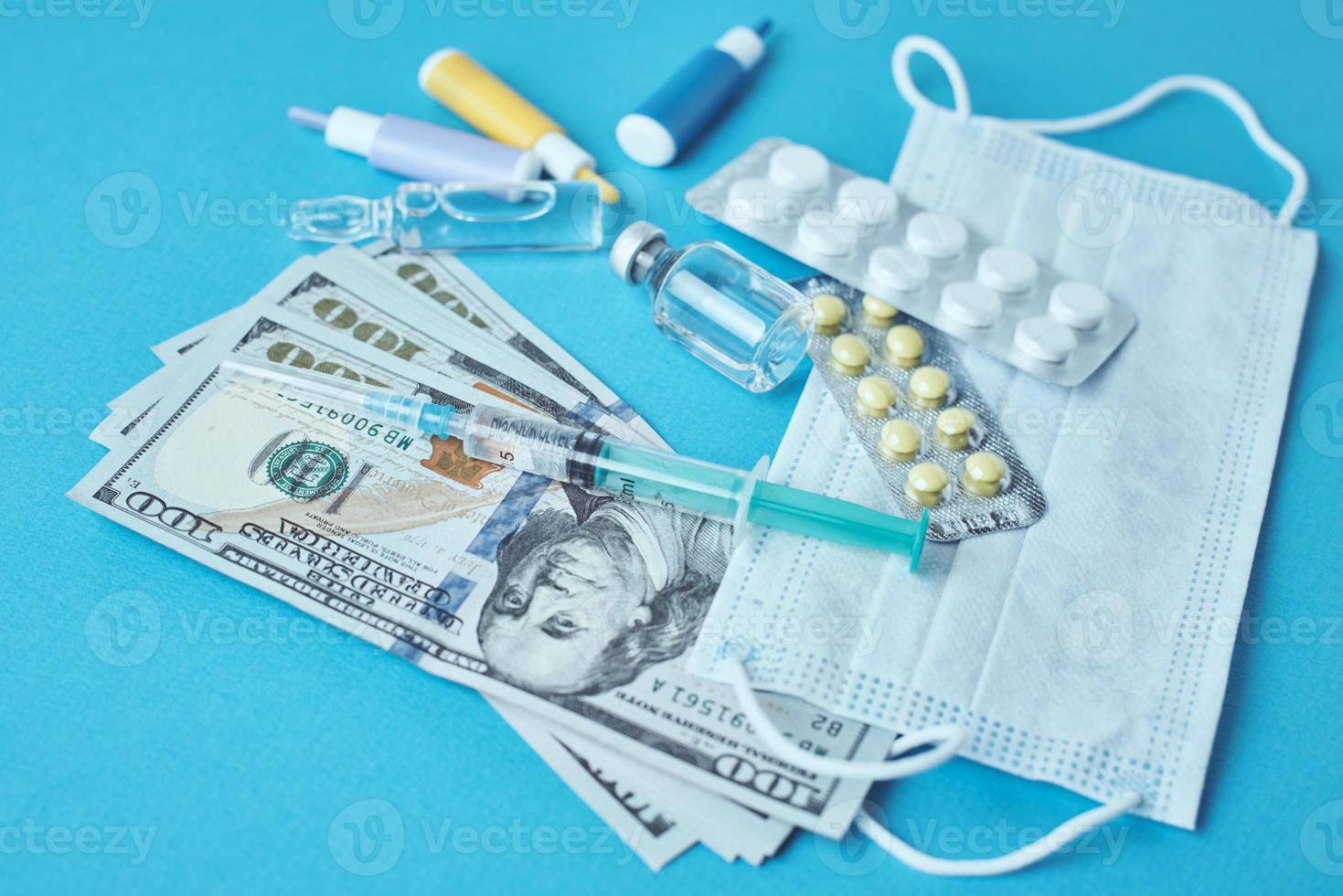 pastillas, máscara protectora, artículos médicos y billetes de dólar en el fondo azul foto
