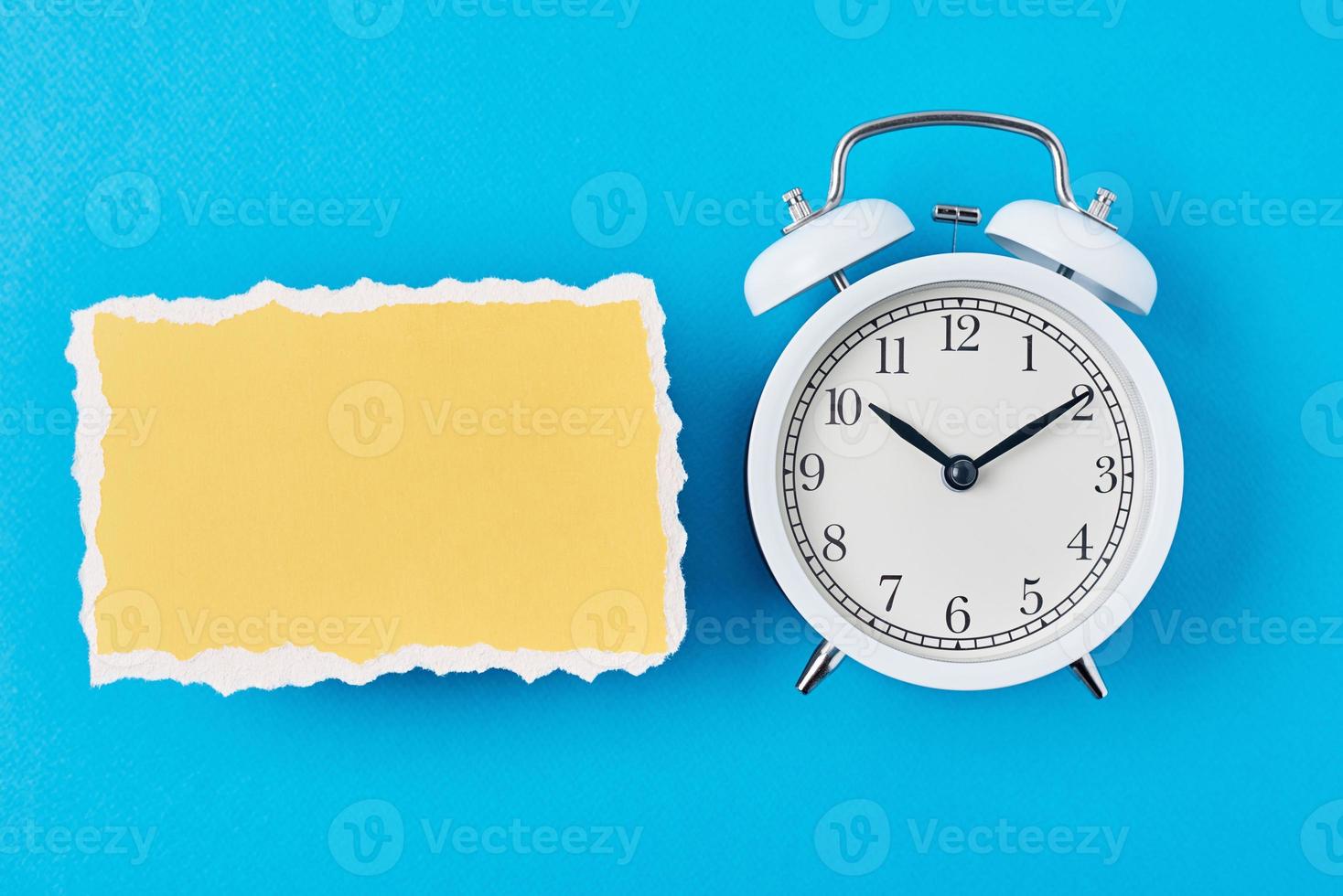 despertador blanco y hoja de papel rota vacía sobre un fondo azul foto