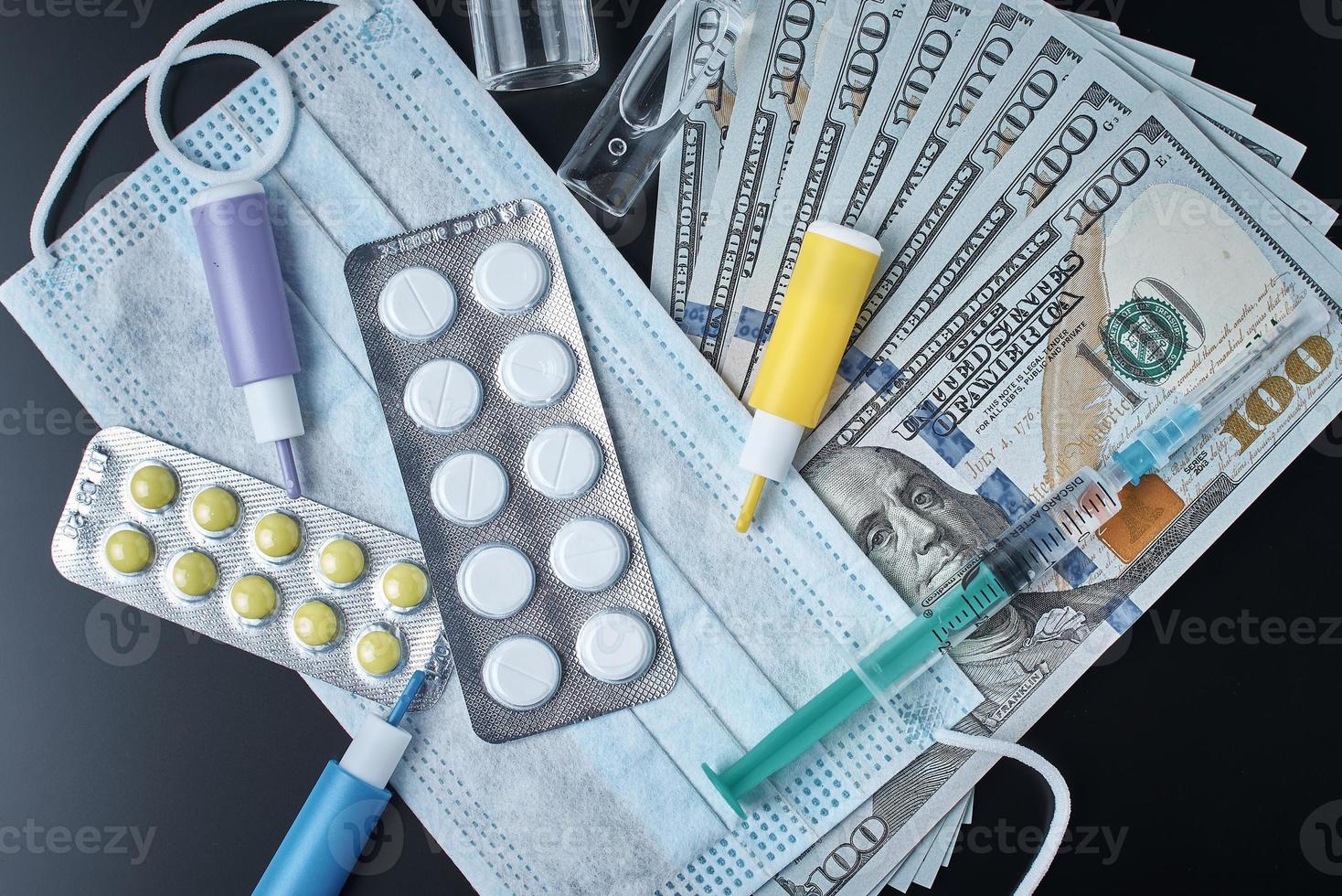 Tablets, protective mask, medical items and dollar bills on dark background photo