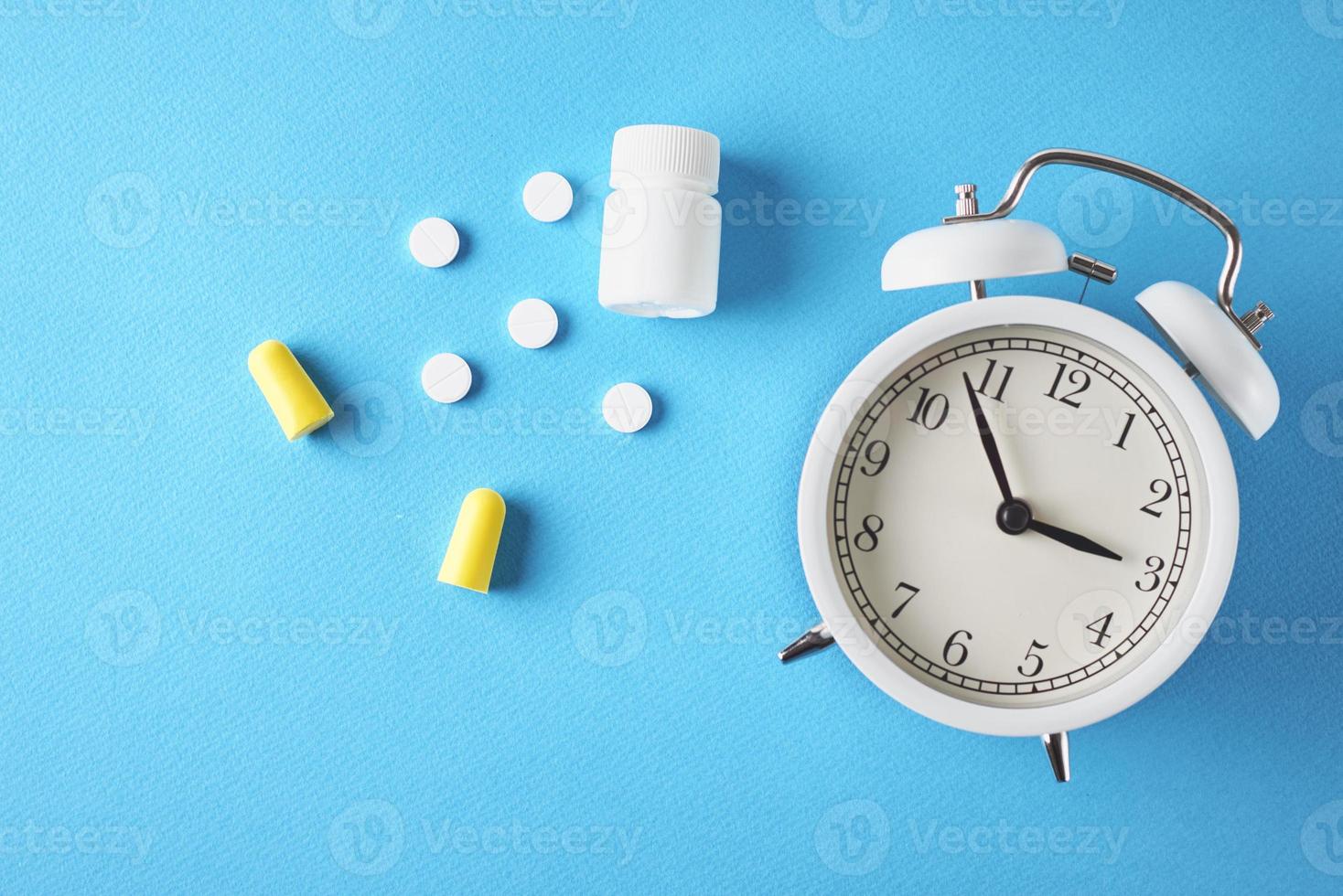 Insomnia problem concept. Alarm clock, ear plugs and pills on a blue