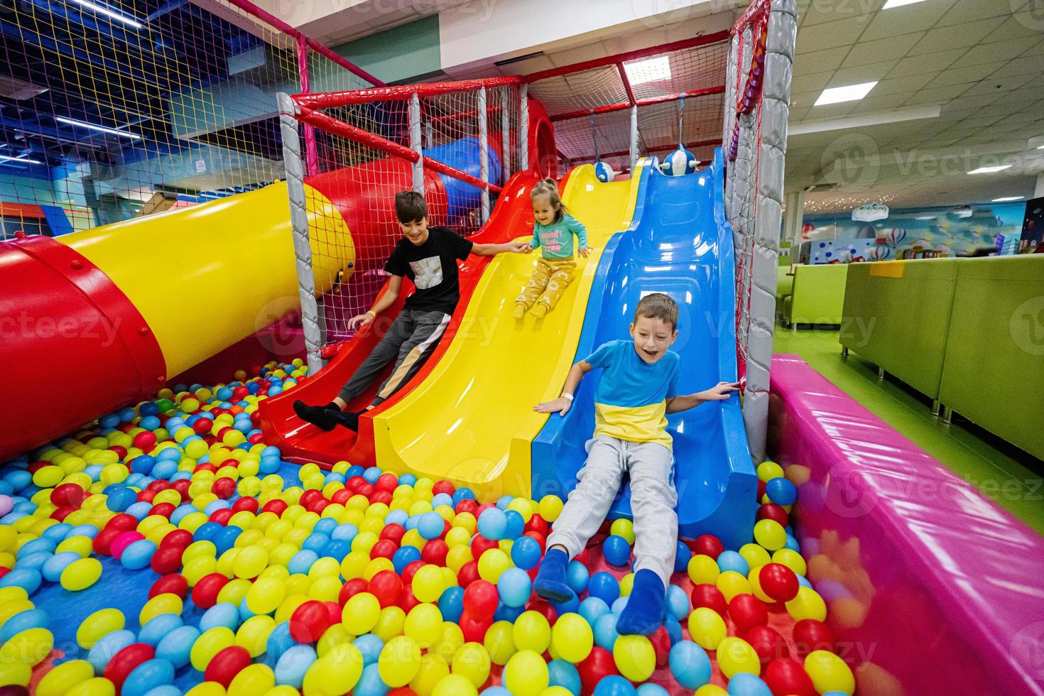 Happy kids playing at indoor play center playground. Children slides in colored slide into balls