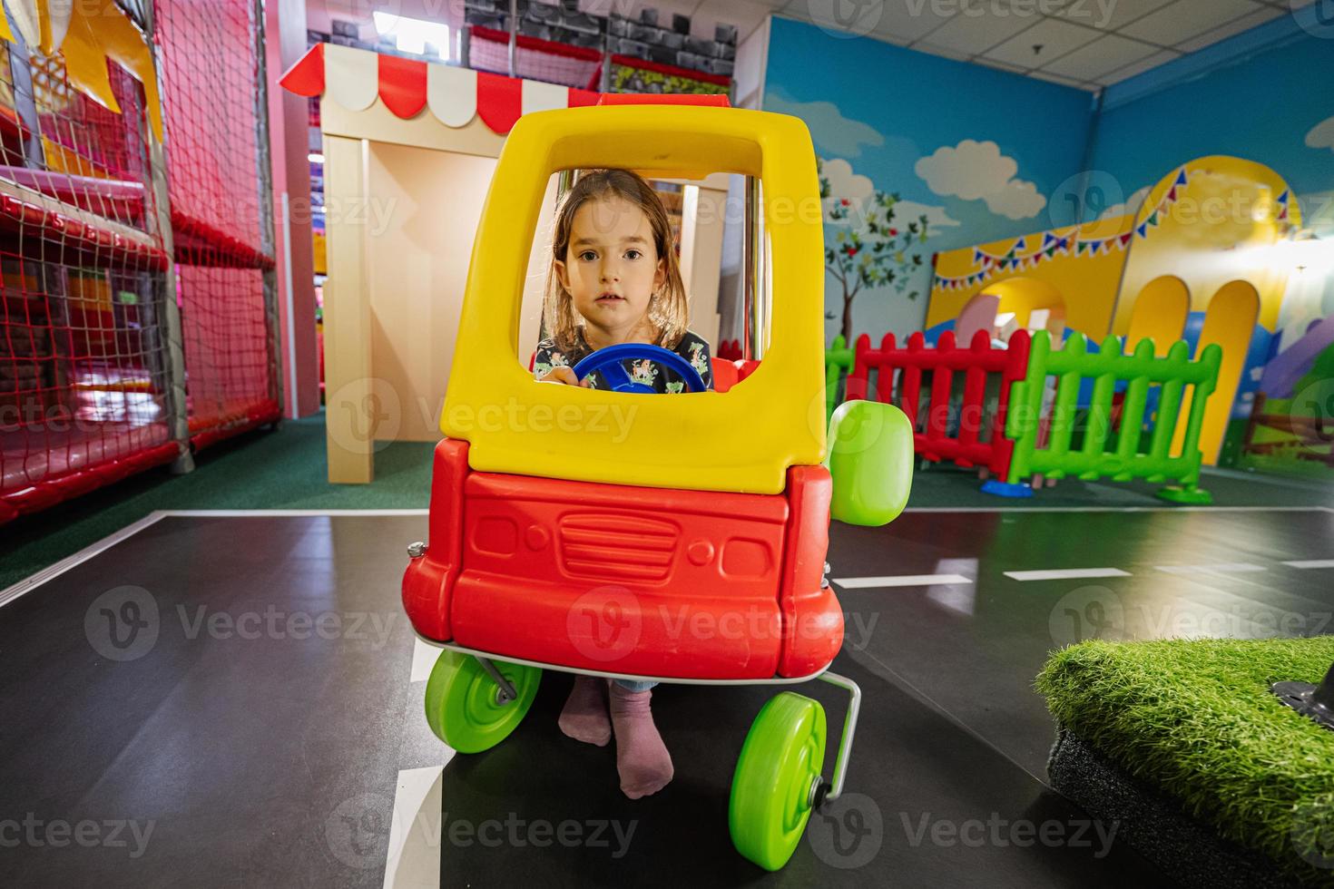 niños jugando en el patio interior del centro de juegos, niña en coche de juguete. foto