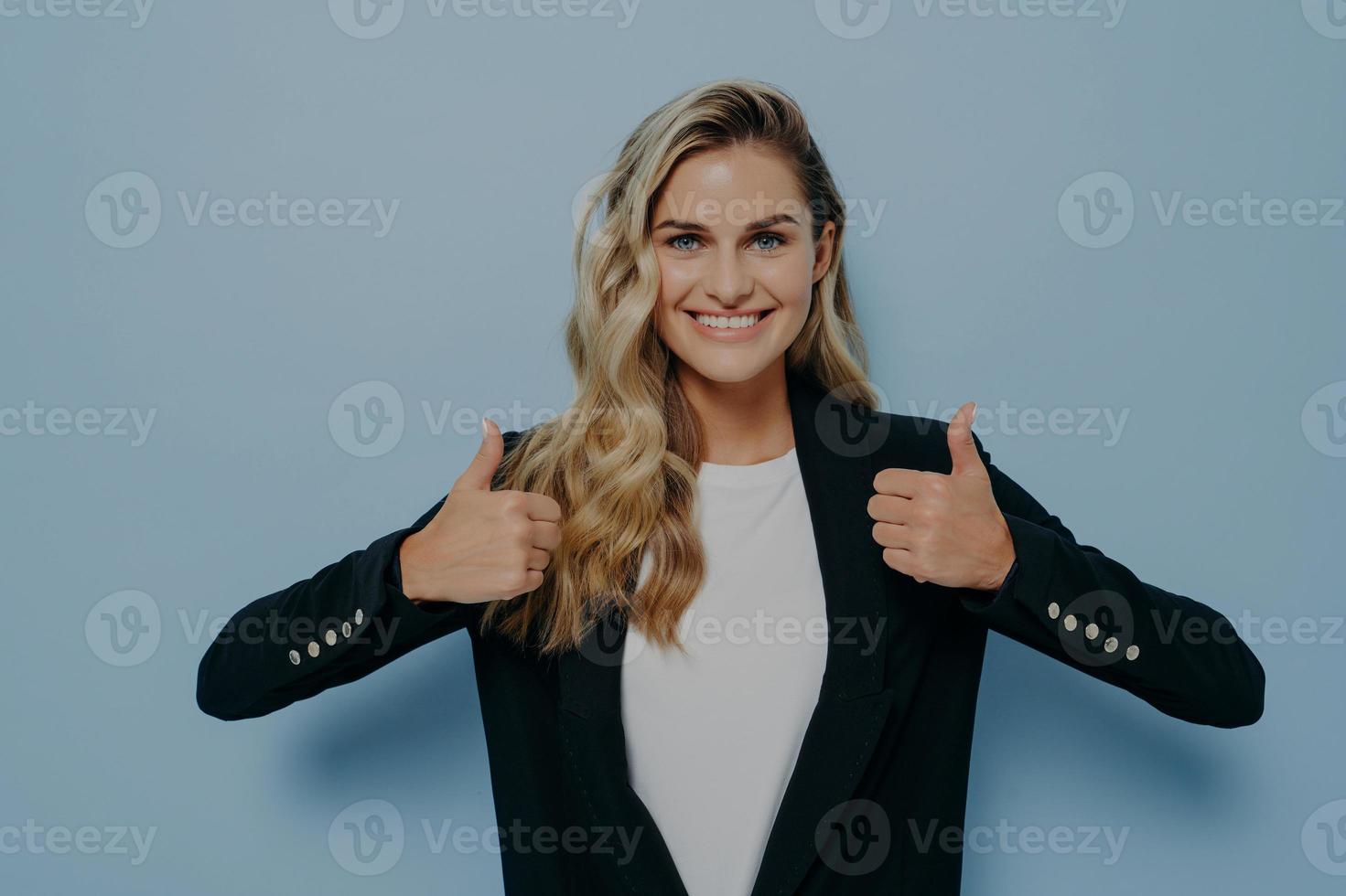 Cheerful girl with blonde hair looking at camera with satisfaction, smiling and showing thumbs up photo