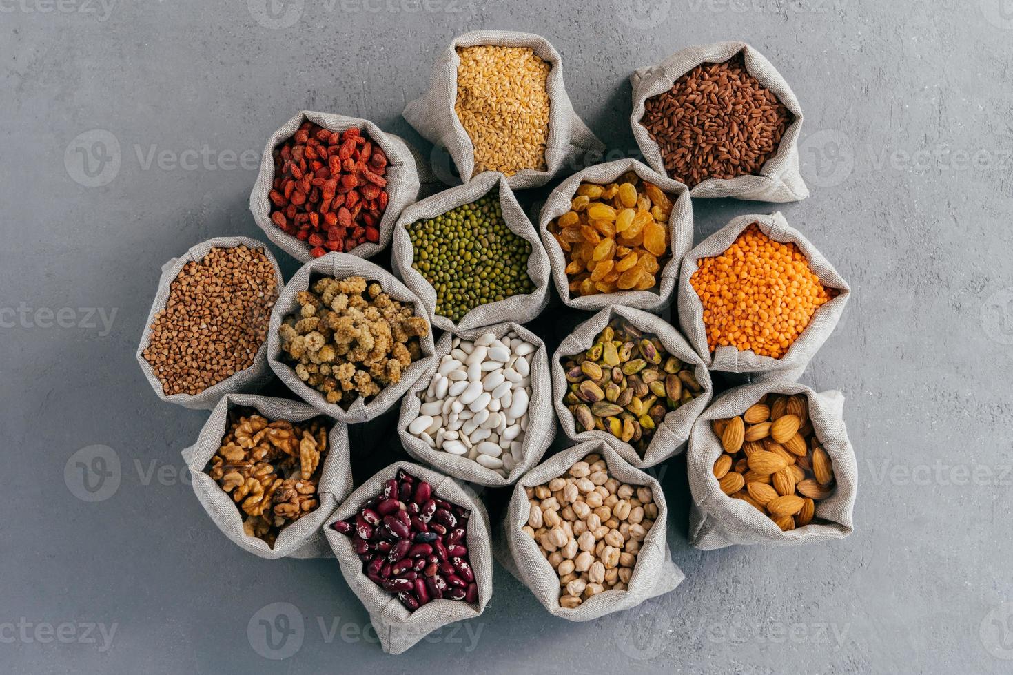 Natural cereal food concept. Top view of little cloth sacks stand around, consisted of healthy dried fruit and cereals. Mixed variety. Flat lay photo