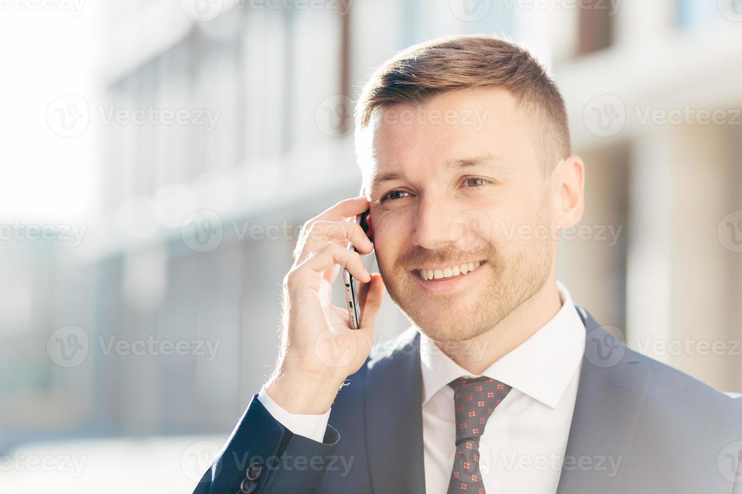 Confident happy middle aged businessman communicates via cell phone, discusses financial report with business partner, wears formal clothes, stands outdoor against blurred background. Busy CEO photo