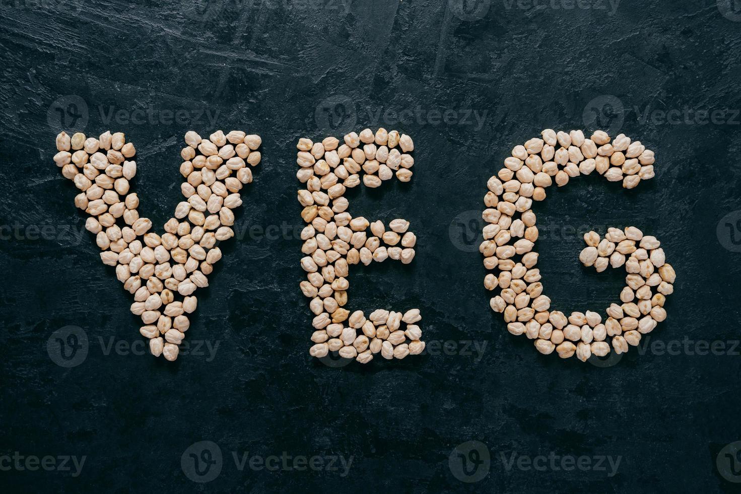 Uncooked chickpeas shaped in letters veg, isolated over dark background. Vegetarianism and healthy eating concept. Healthy nutrition photo