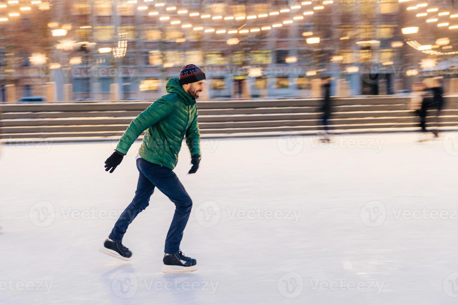 Middle aged male wears figure skates, being at ice rink in winter park, has fun with friend. Athlete speed skater demonstrates his talents on skating ring. Winter sport. Christmas vacations. photo