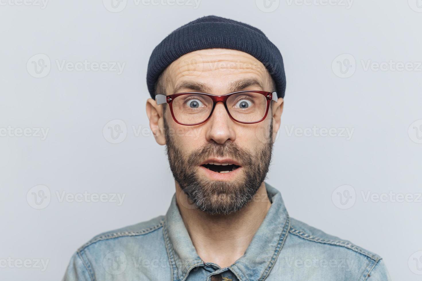 Horizontal shot of amazed excited shocked man stares at camera with unexpected expression, keeps mouth opened, hears awful news, isolated over grey background. Omg and great surprisment concept photo