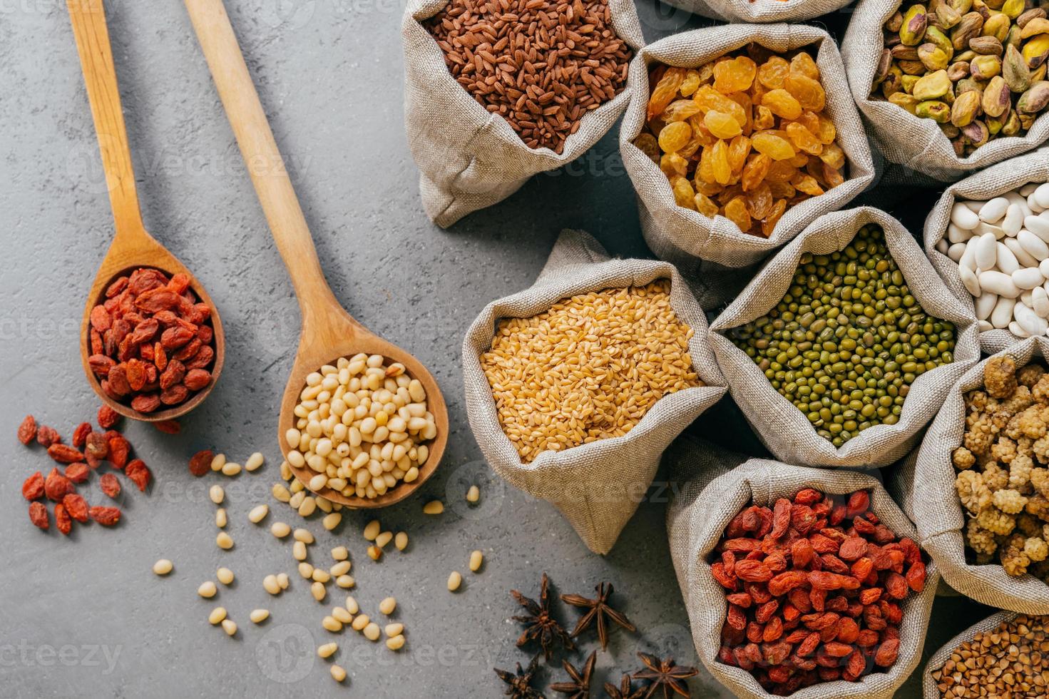 Small sacks with various dried fruit and cereals packed. Two wooden spoons on grey background. Healthy legumes and grains photo