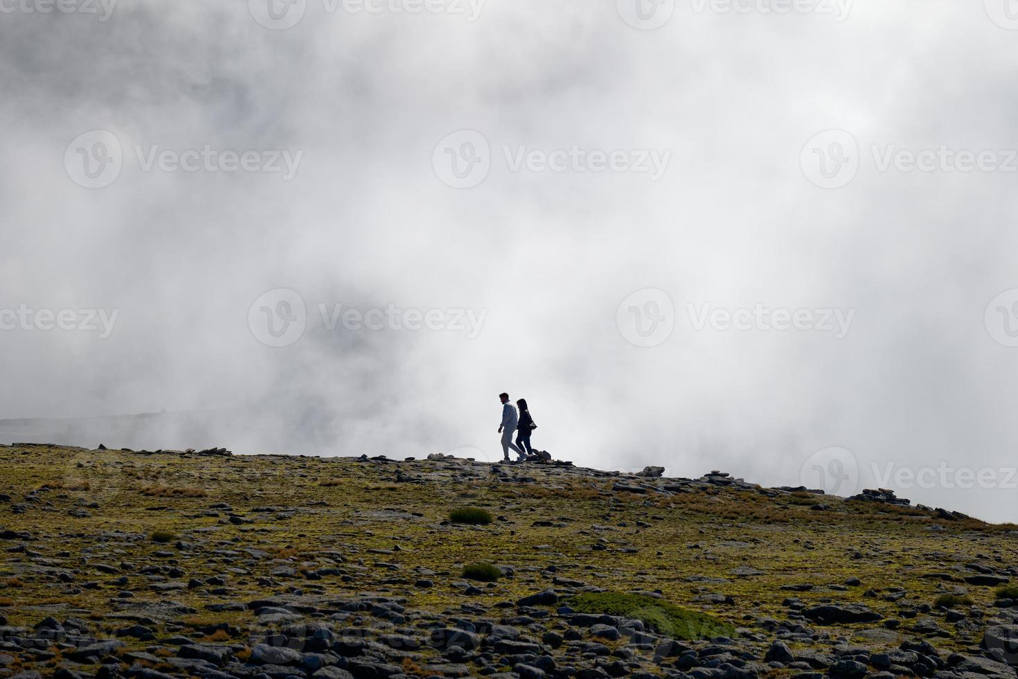 Tourists walking on the top of Serra da Estrela, the highest mountain of continental Portugal with thick clouds around. Travel and explore. People on the peak of the mountain. photo