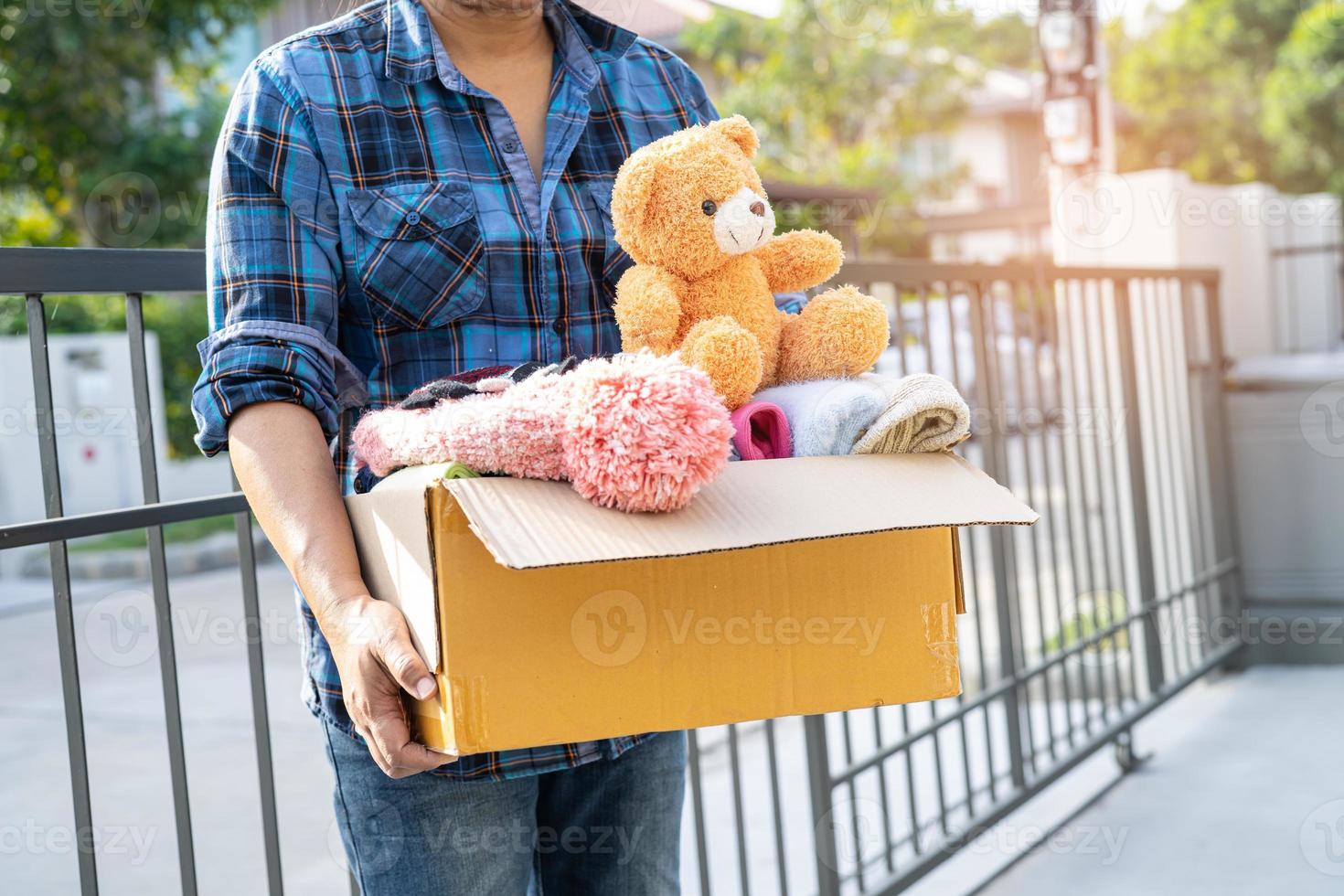 Holding clothing donation box with used clothes and doll at home to