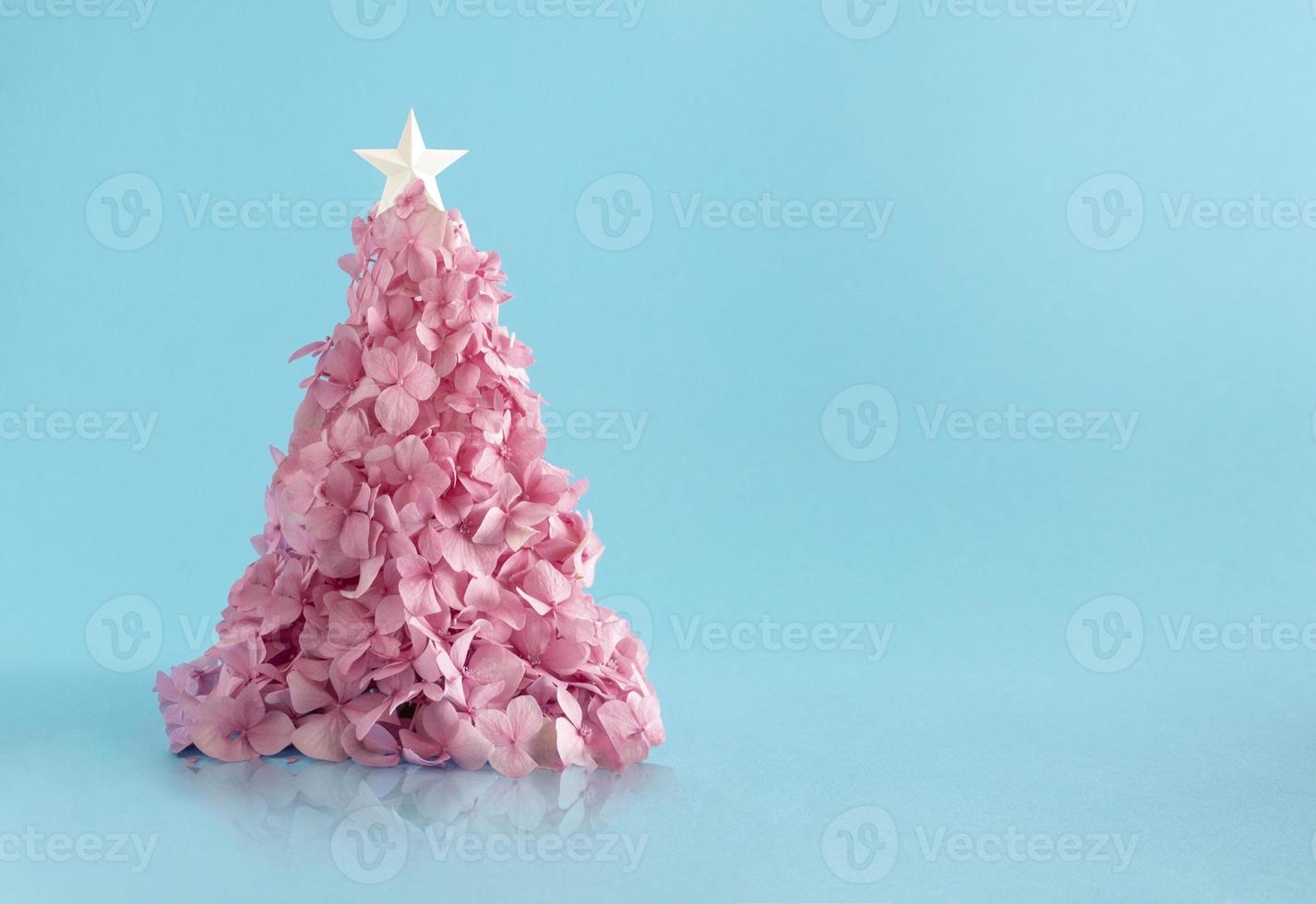 Christmas tree made of a small pink flowerers against light blue background. Minimal flat lay composition. photo