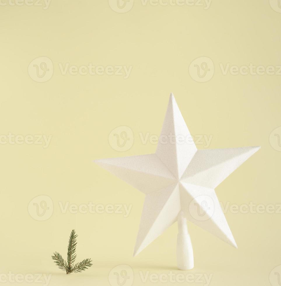 Big white star and small fir branch standing next to each other against yellow background. Minimal Christmas concept. with copy space. photo